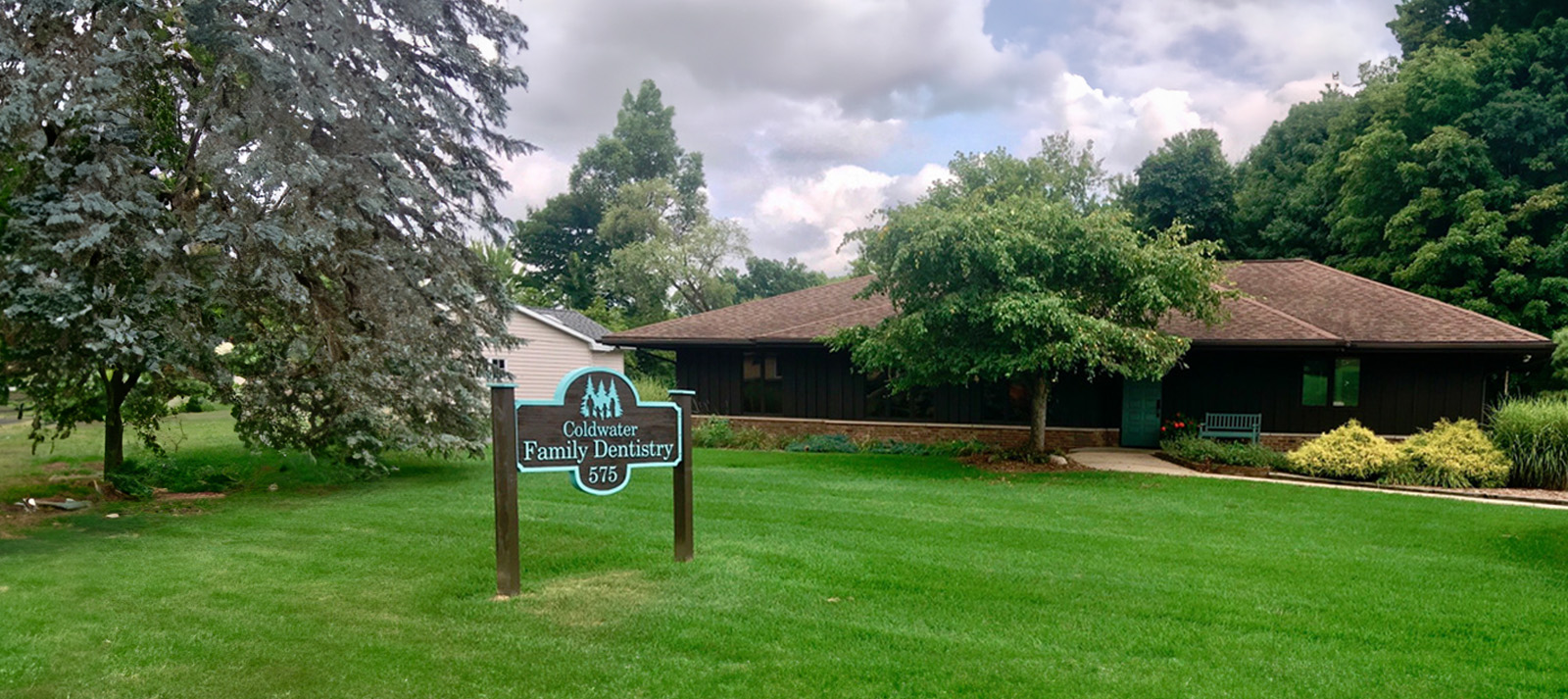 The image shows a sign in the foreground and a building with trees behind it.