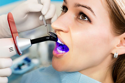 A woman receiving a dental cleaning with a device that appears to be a digital or advanced dental tool, accompanied by a dental hygienist wearing protective gloves and a mask.