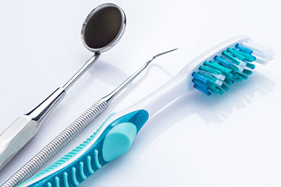 Image of dental tools including a toothbrush, dental mirror, tweezers, and scissors on a white background.