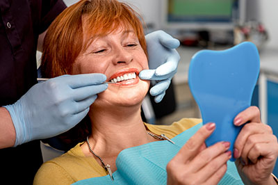 The image shows a woman sitting in a dental chair, having her teeth cleaned by a dentist who is using a toothbrush and a blue mouthguard.