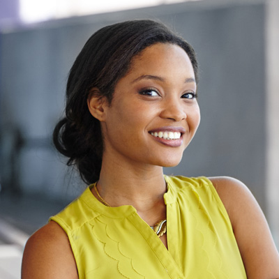 Smiling woman in a yellow top against a blurred background.