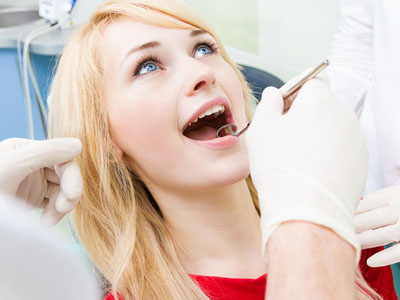 A young woman in a dental chair receiving dental care, with a dental professional assisting.