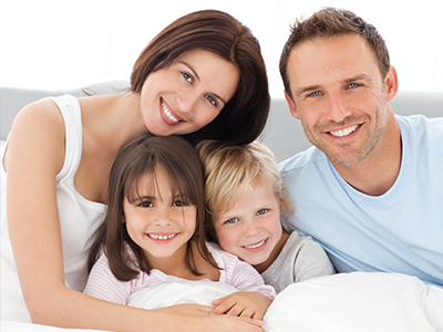 A family of four, including two adults and two children, poses for a photo in bed.